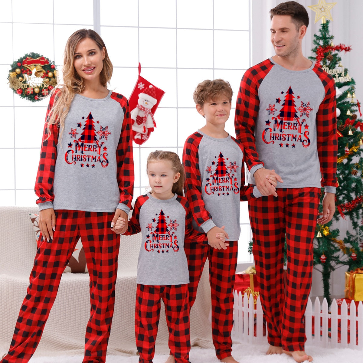 Full shot of a family (parents, toddler, baby) in red plaid Christmas pajamas, celebratory holiday wear.