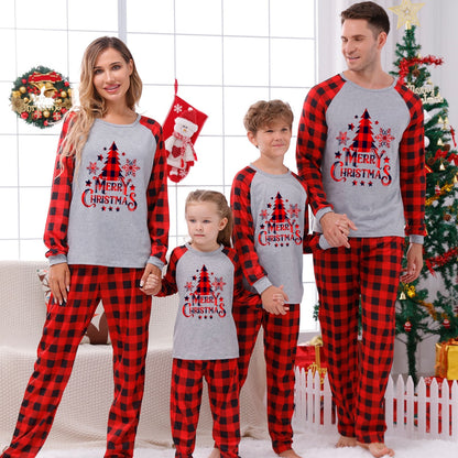 Full shot of a family (parents, toddler, baby) in red plaid Christmas pajamas, celebratory holiday wear.