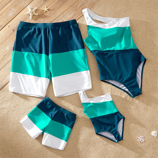 Family matching color block swimsuits with father, mother, and child posing on a beach at sunset