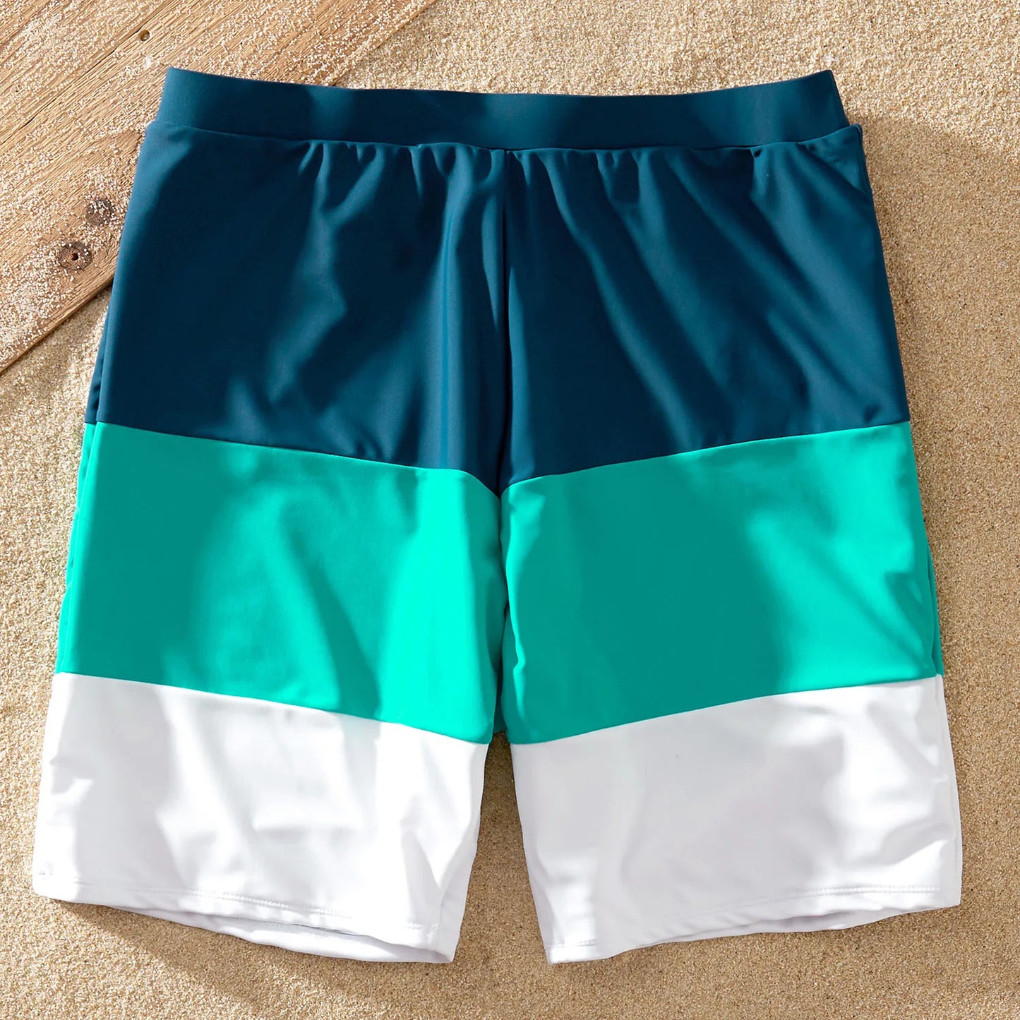 Father and son in matching color block swim trunks and rash guard during a family beach vacation