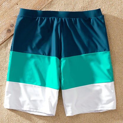 Father and son in matching color block swim trunks and rash guard during a family beach vacation