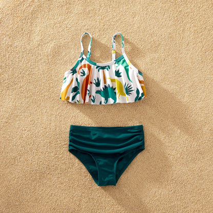 Family matching dinosaur swimsuits modeled on a sandy beach, showcasing summer fashion.
