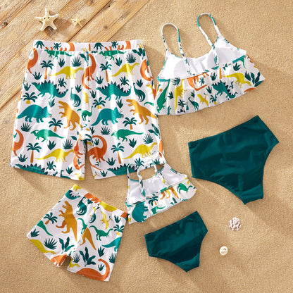Children building sandcastles in their blue dinosaur print swimsuits, beach playtime.