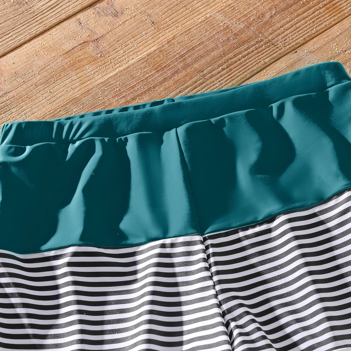 Collection of family swimwear: green one-shoulder swimsuit, striped trunks, vacation essentials