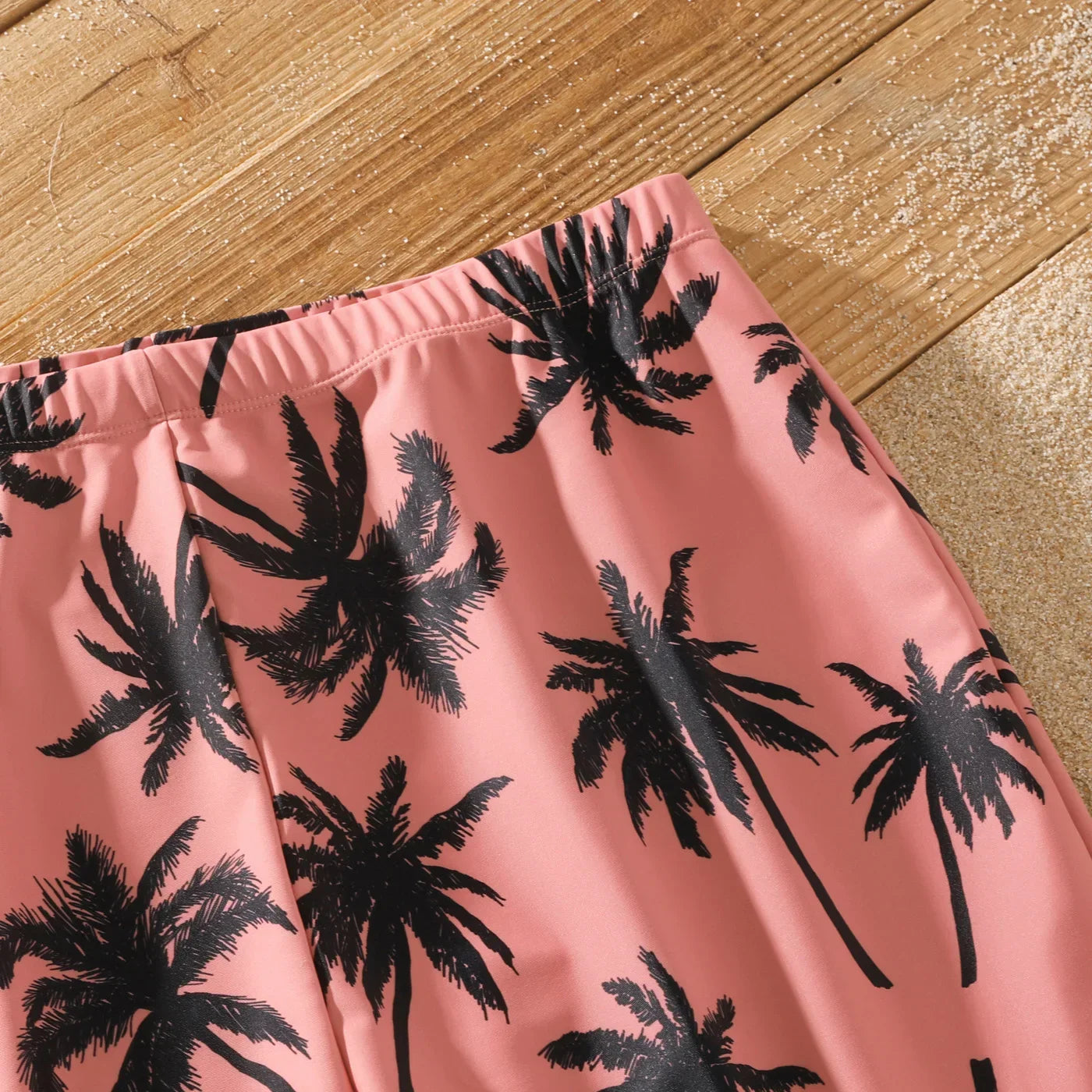 Boy's pink swim shorts with coconut tree design, ideal for family beach day