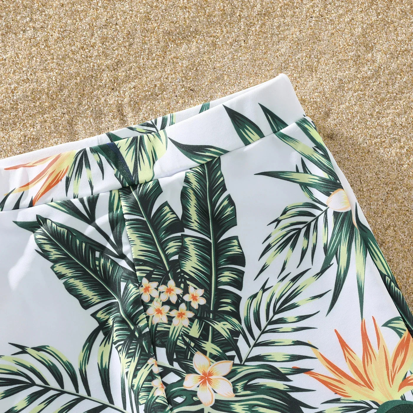 Happy family walking hand-in-hand on the beach in their matching plant print swimming outfits