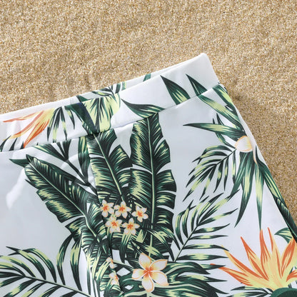 Happy family walking hand-in-hand on the beach in their matching plant print swimming outfits