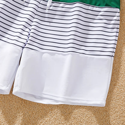 Family silhouettes by the ocean, all wearing matching green striped swimsuits