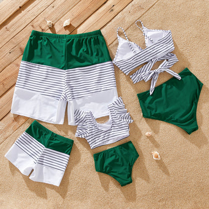 Mom, dad, and child wearing green striped matching swimwear for family beach day