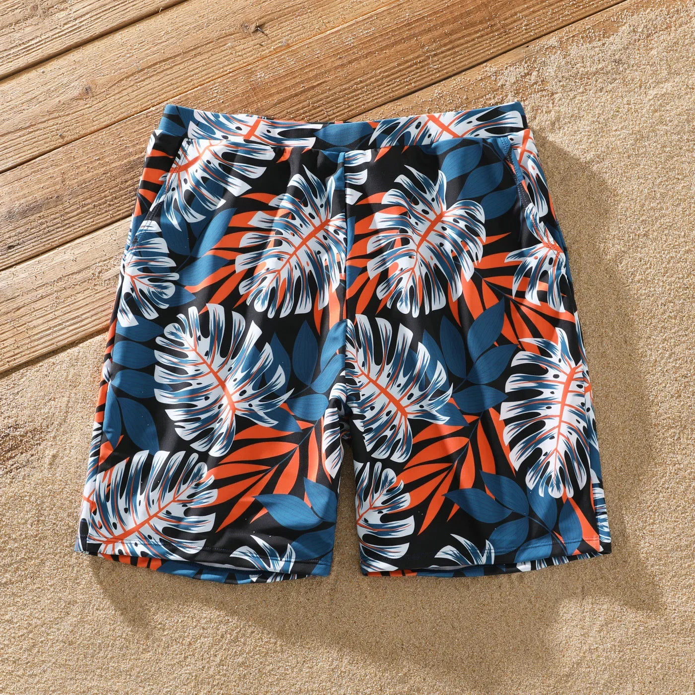 Full family wearing coordinated palm leaf print swimwear on a sandy beach