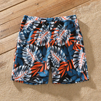 Full family wearing coordinated palm leaf print swimwear on a sandy beach