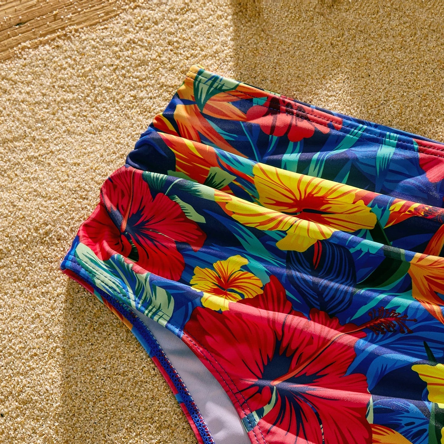 Scallop detail on a women's one-piece swimsuit, paired with men's tropical floral swim shorts.