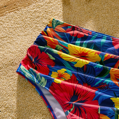 Scallop detail on a women's one-piece swimsuit, paired with men's tropical floral swim shorts.