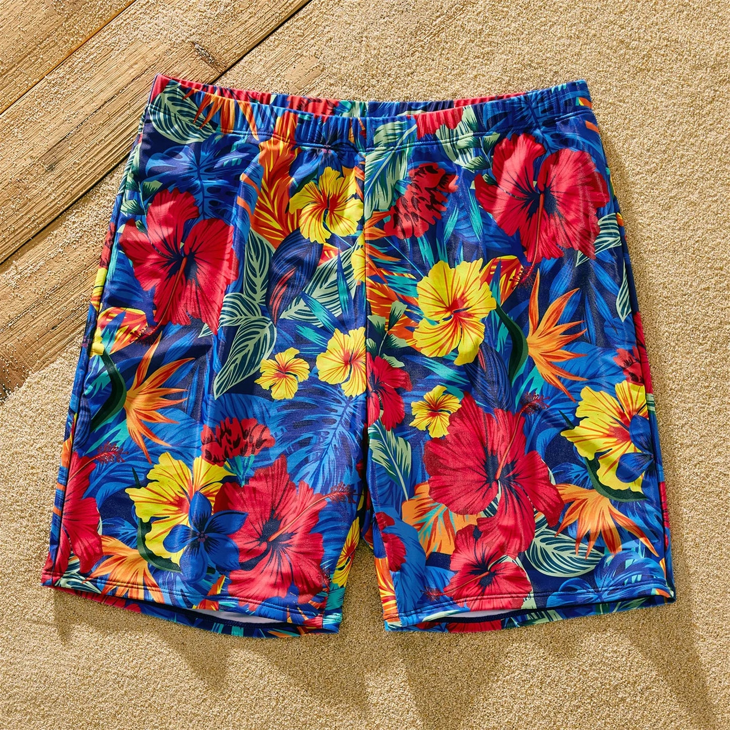 Family posing on a beach, all wearing matching scallop trim women's swimsuits and floral trunks.