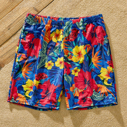 Family posing on a beach, all wearing matching scallop trim women's swimsuits and floral trunks.