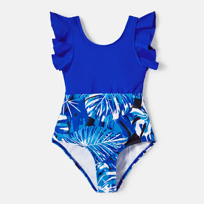 Mother and daughter in matching tropical leaf ruffle swimsuits, posing happily outdoors.