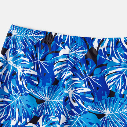 Assortment of family matching tropical leaf swimwear: men's trunks, women's & girls' ruffle swimsuits.