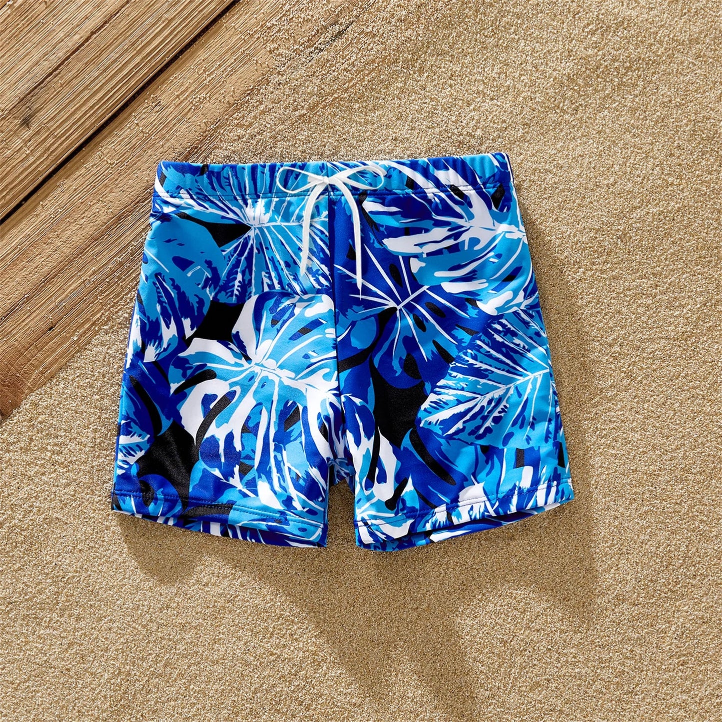 Full shot of family, all wearing coordinating tropical leaf print swimwear, laughing by the ocean.