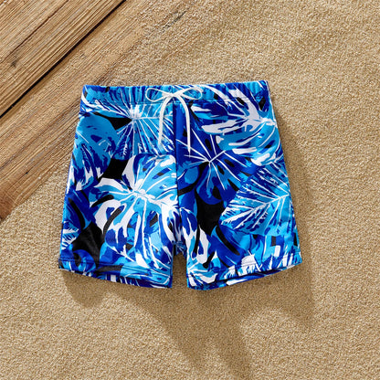Full shot of family, all wearing coordinating tropical leaf print swimwear, laughing by the ocean.