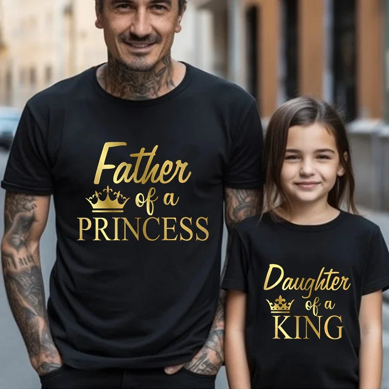 Father and daughter wearing 'Princess King' matching t-shirts, enjoying family time outdoors.