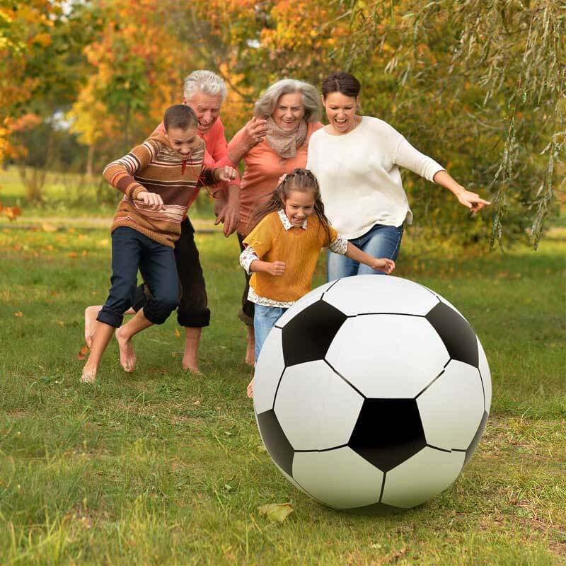 Kids and adults playing with a giant black and white inflatable soccer ball on a sunny beach