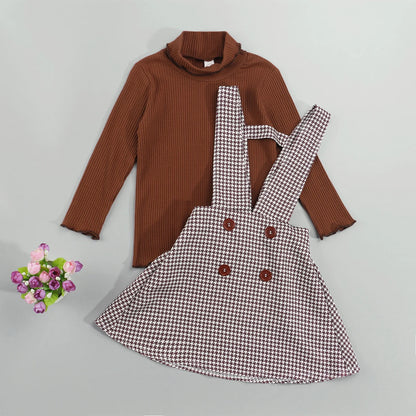 Girls autumn two-piece set featuring a cream turtleneck top and a pleated plaid suspender skirt.