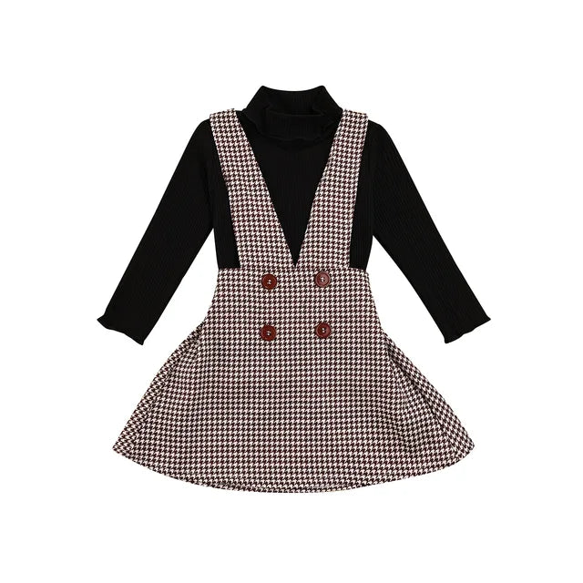 Full view of a girls' autumn outfit: a solid turtleneck and a stylish plaid suspender skirt for kids.