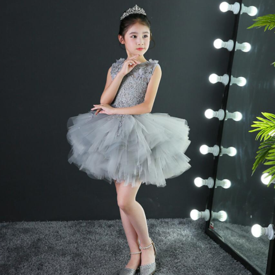 Young girl twirling in a long, flowing pink tulle princess gown with delicate lace appliques, ideal for parties