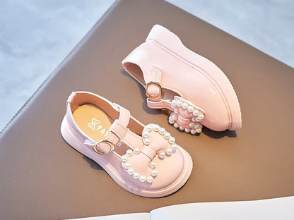 Close-up of the bow-knot and pearl embellishment on girls pink princess flats, intricate detail.