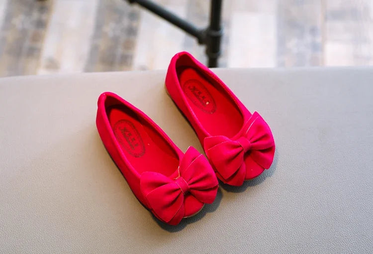 Girls' pink bowtie slip-on sandals on a sandy beach, ready for summer fun and holidays