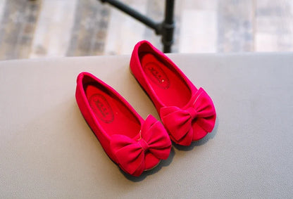 Girls' pink bowtie slip-on sandals on a sandy beach, ready for summer fun and holidays
