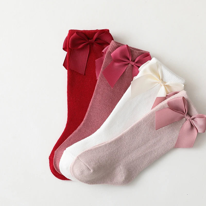 Toddler girl wearing white cotton knee-high bow socks; comfortable summer kids' fashion