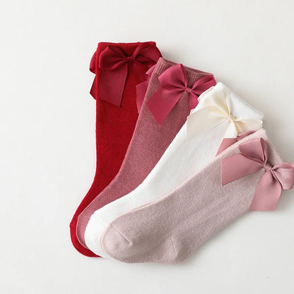 Toddler girl wearing white cotton knee-high bow socks; comfortable summer kids' fashion