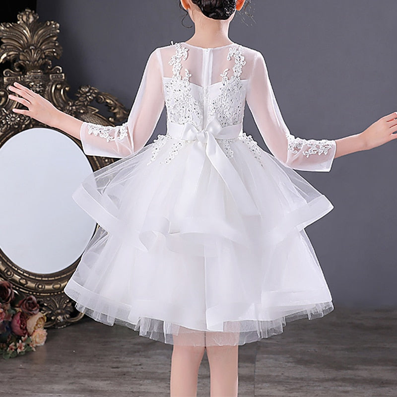 Close-up of the delicate pink beading and lace detail on a girls' white party dress, long sleeve.