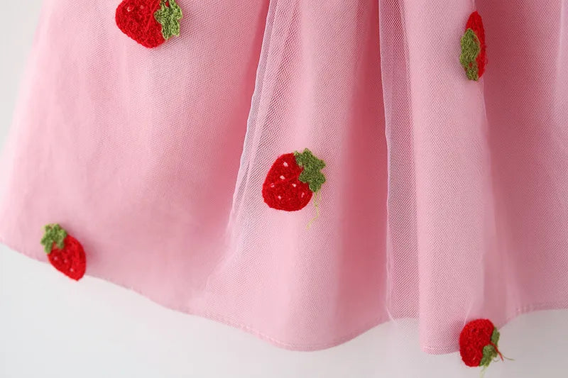 Soft white toddler dress with playful strawberry embroidery and a small decorative bow.