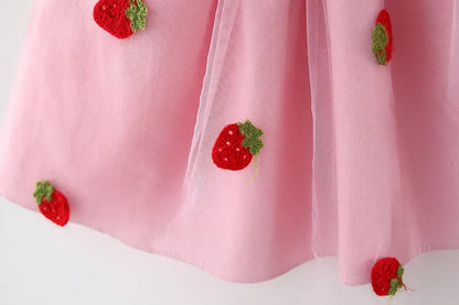 Soft white toddler dress with playful strawberry embroidery and a small decorative bow.