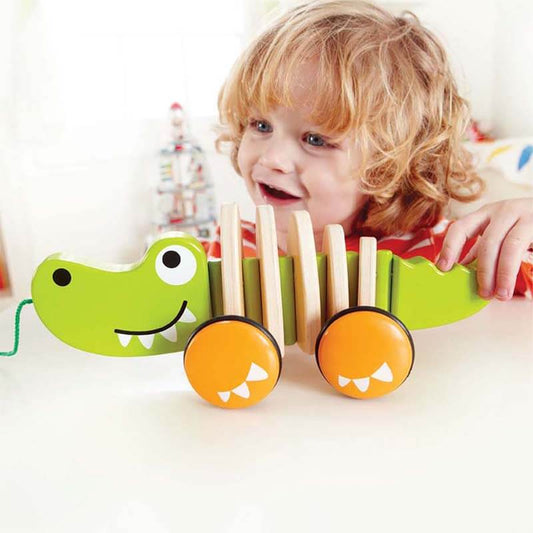 Green wooden crocodile pull-along toy for toddlers, with wheels and string, on a light background.