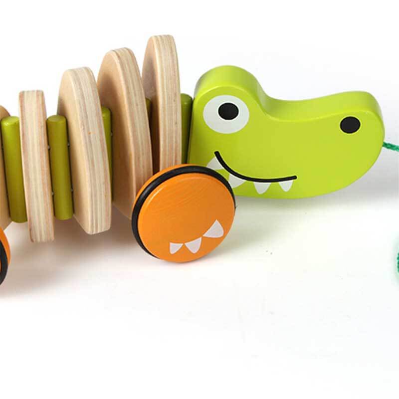 Close-up of a child's hand pulling a developmental wooden crocodile toy with rotating wheels.