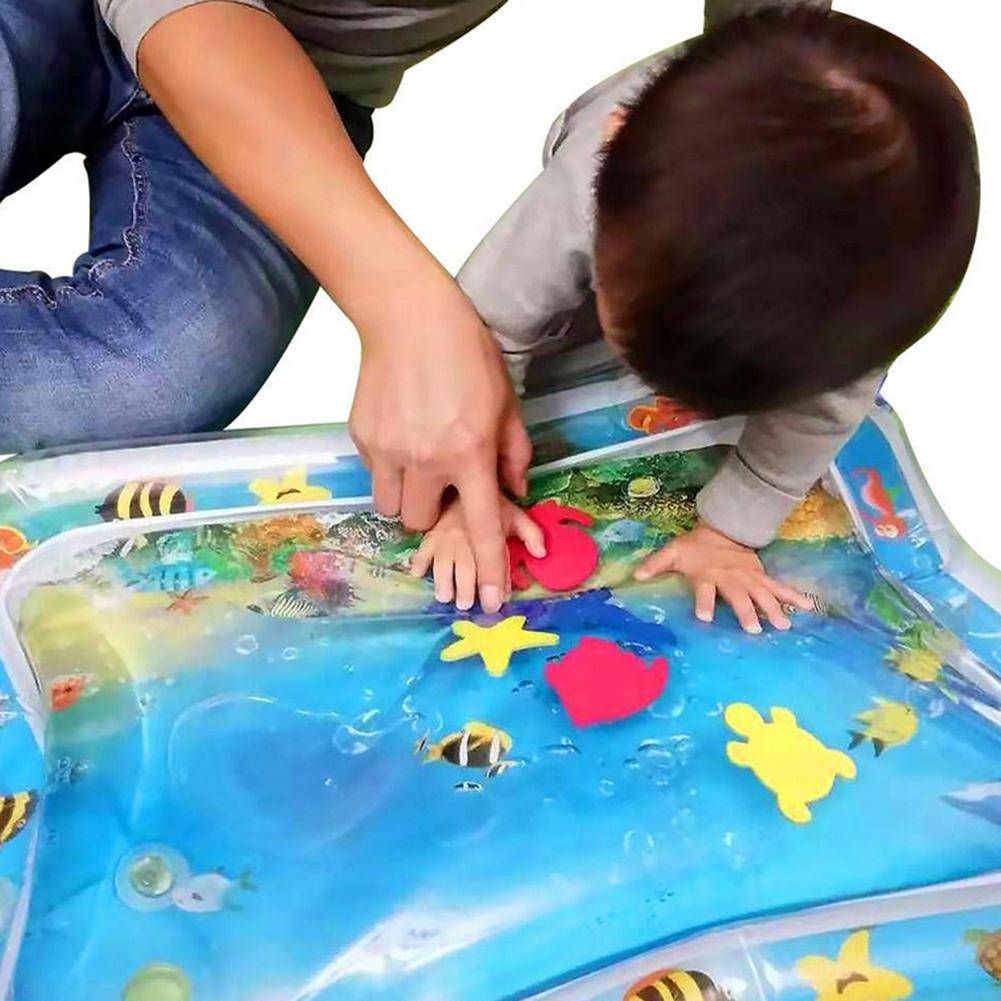 Close-up of a baby's hands on a tummy time water mat, interacting with floating toy fish and improving strength.