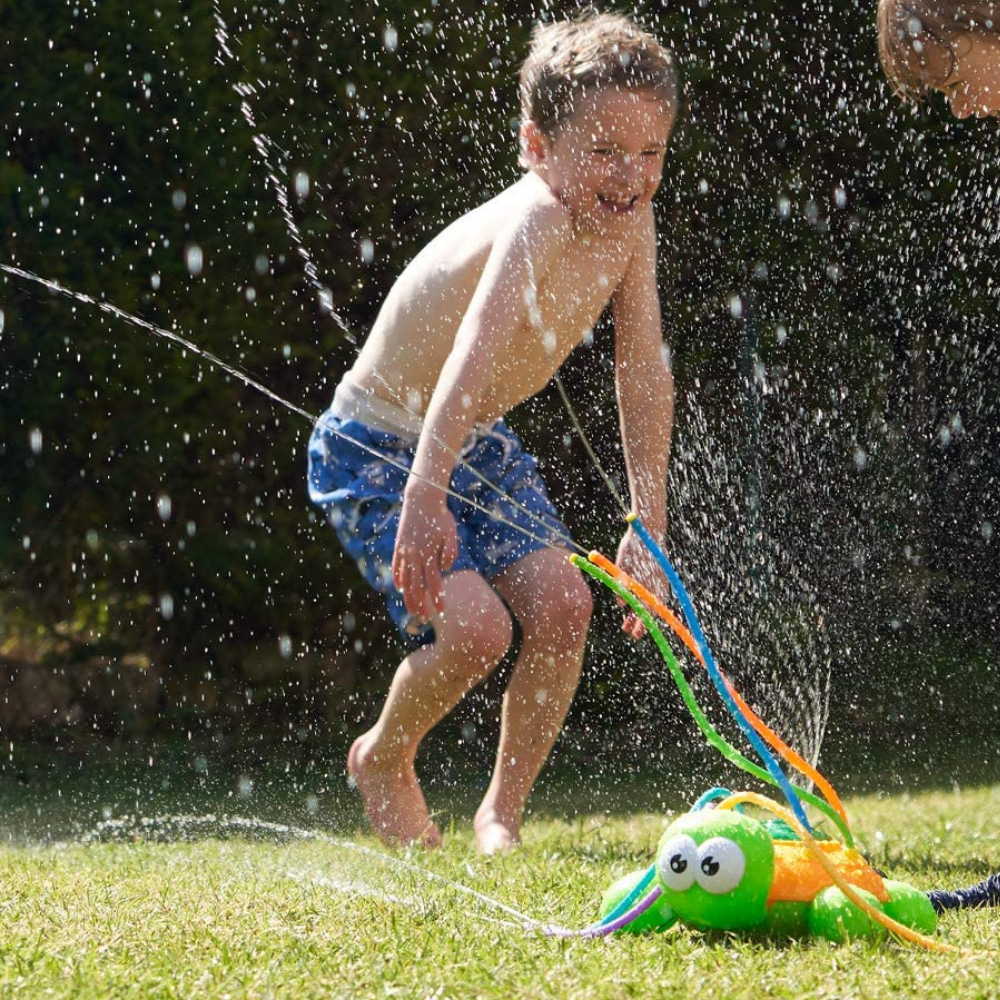 Happy children running through a gentle sprinkler, enjoying outdoor water play in a green backyard on a warm day.