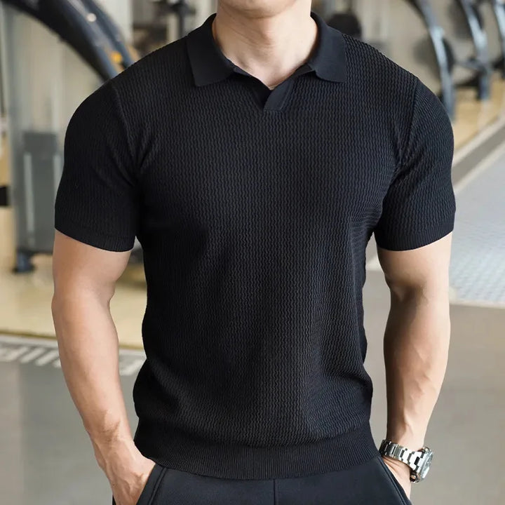 Model wearing a men's slim fit textured polo shirt, short sleeve, in a relaxed casual setting. Smart daily fashion.