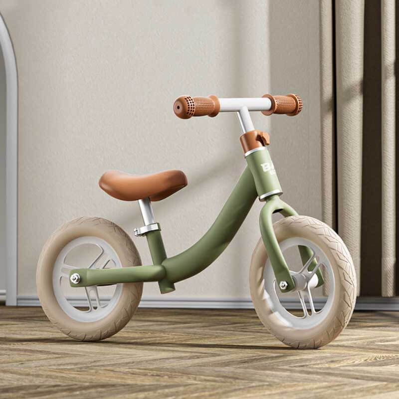 Toddler on a mint green balance bike, riding outdoors, learning to steer and balance.