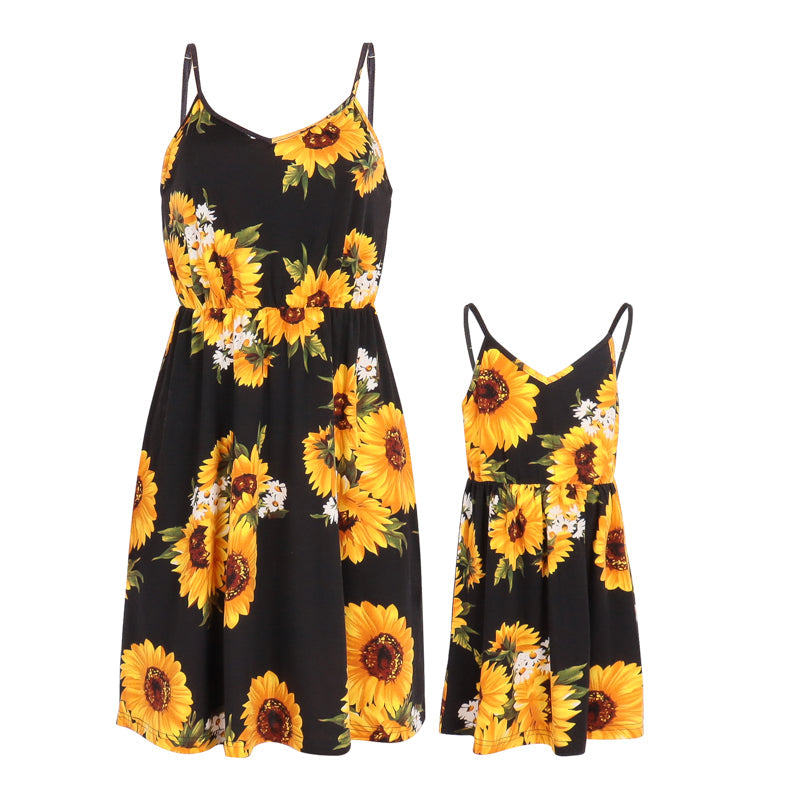 Smiling mother and daughter posing in matching sunflower off-shoulder dresses, family outfits.