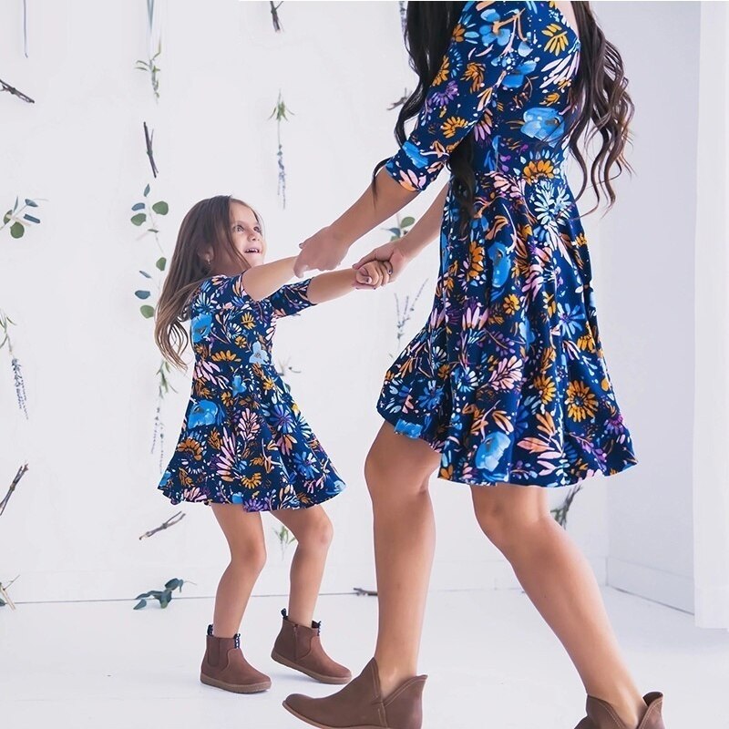 Mother and daughter wearing blue floral dresses, smiling, in a natural setting.