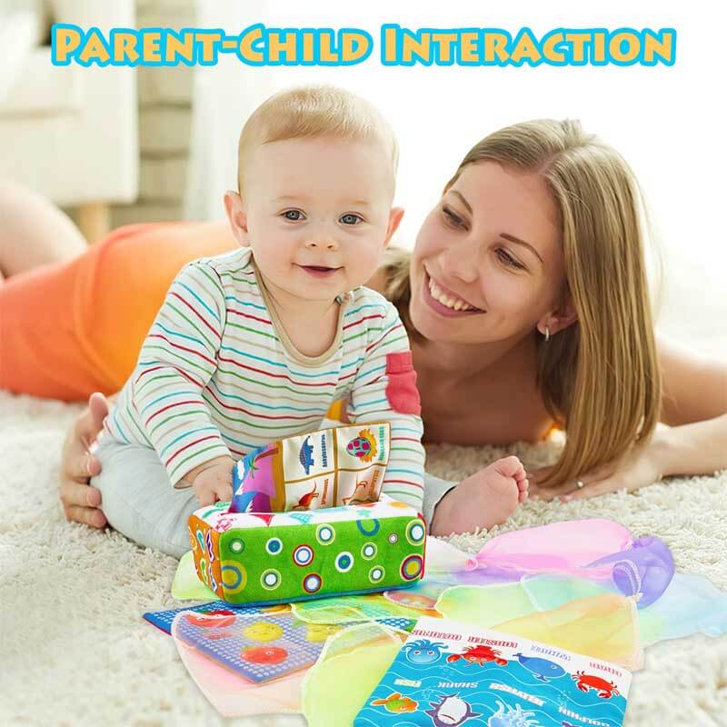 Happy baby interacting with an activity toy: sensory tissue box with crinkle paper and scarves