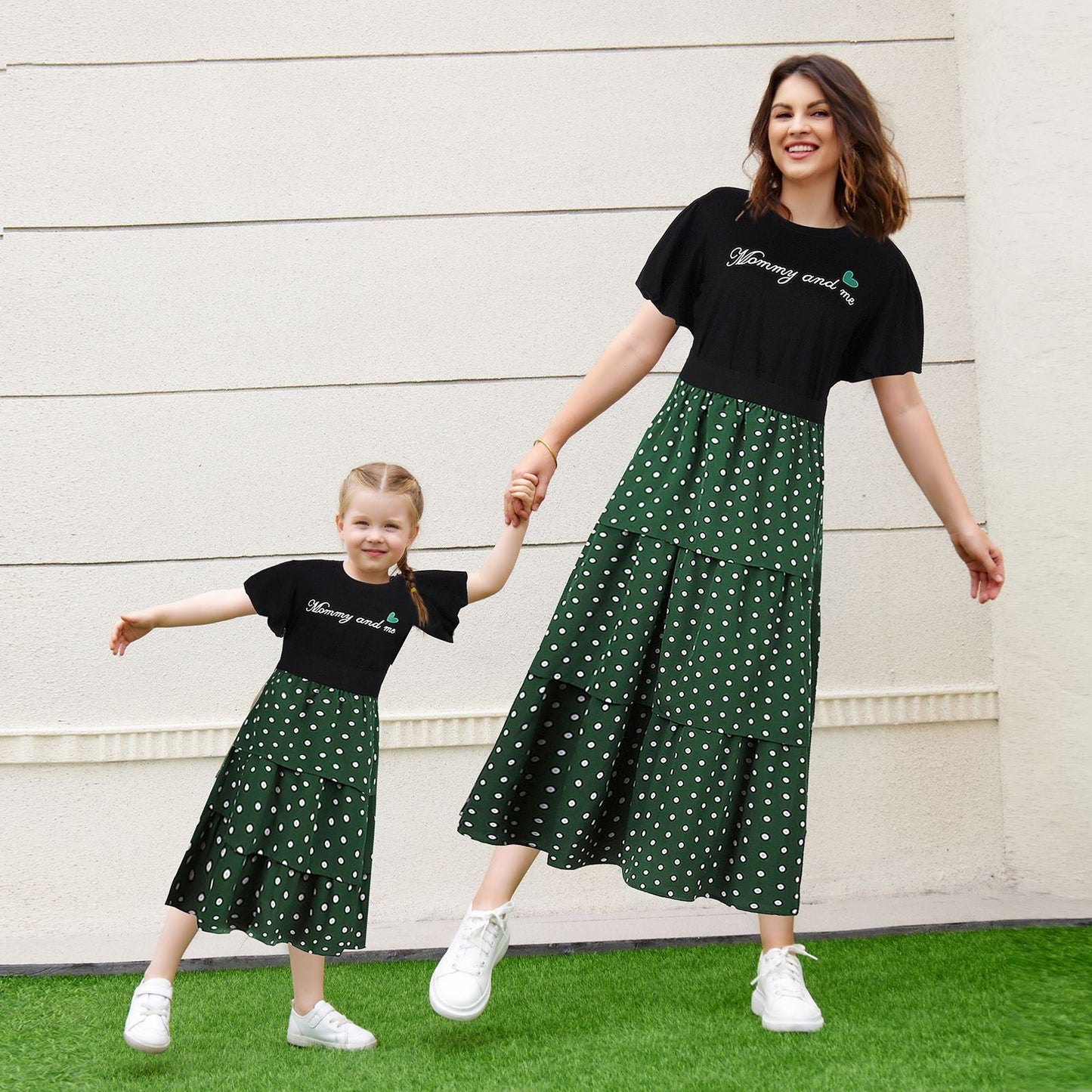 Mother and daughter in matching 'LOVE' letter print shirts and black polka dot skirts, smiling outdoors.