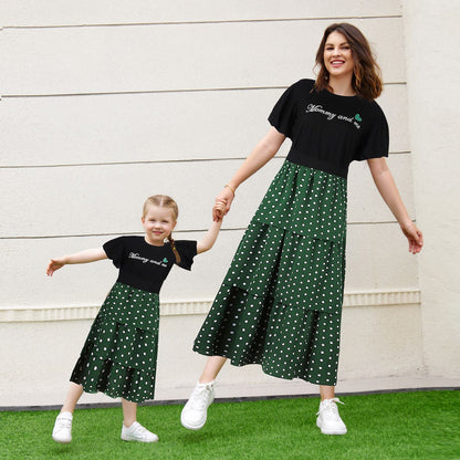 Mother and daughter in matching 'LOVE' letter print shirts and black polka dot skirts, smiling outdoors.