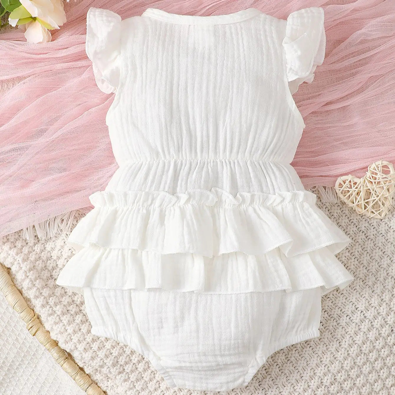 Close-up of white halter dress for newborn baby girl, showing soft cotton fabric and tie-neck detail.