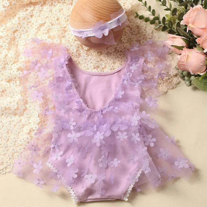 Newborn girl modeling a cute floral romper and headband in a studio setting