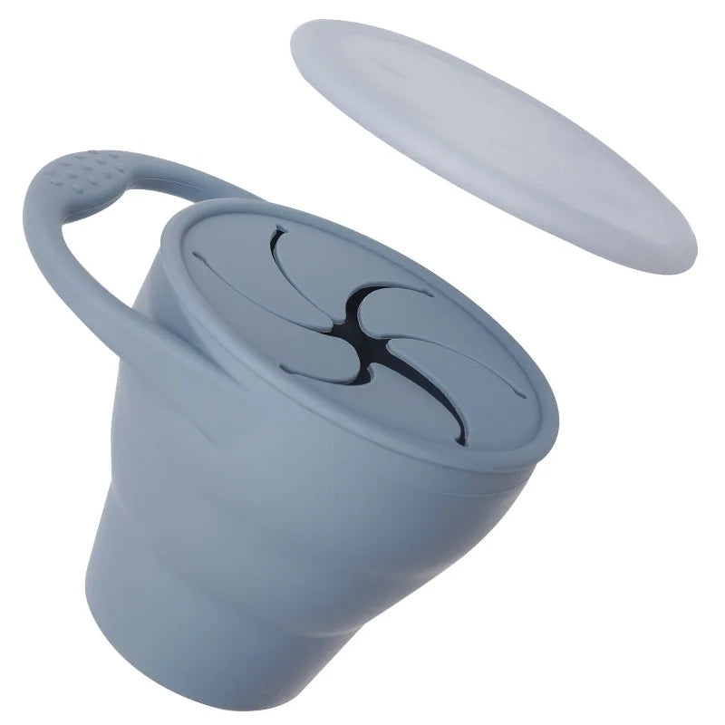 Child's hand holding a blue collapsible silicone snack cup, easy grip design